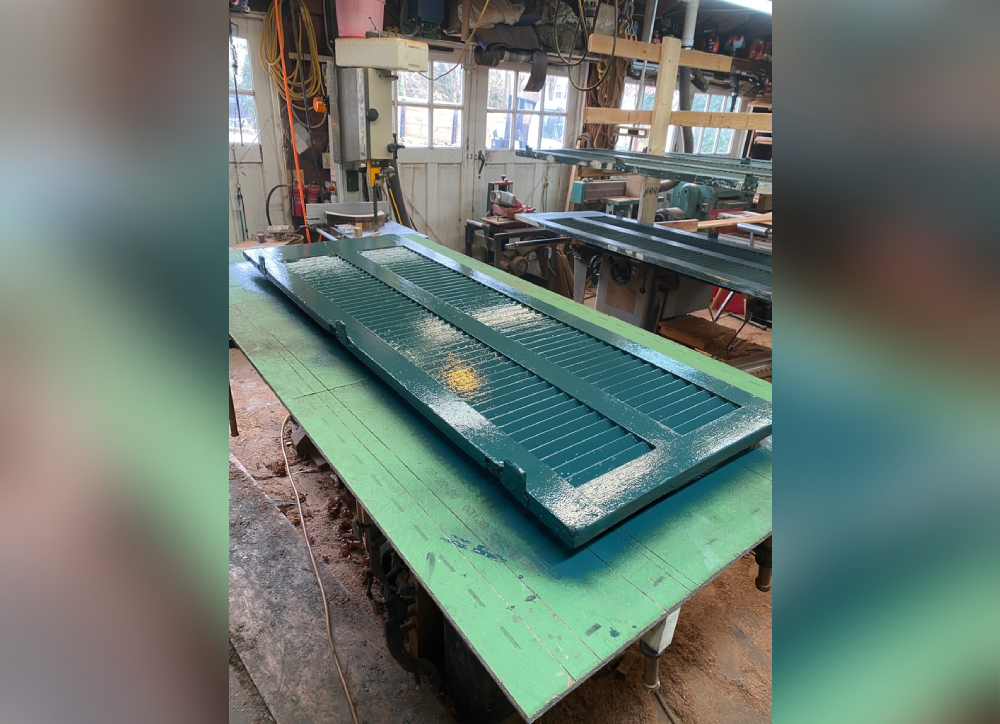 A freshly painted green wooden panel rests on a workbench in a workshop, surrounded by tools and equipment.