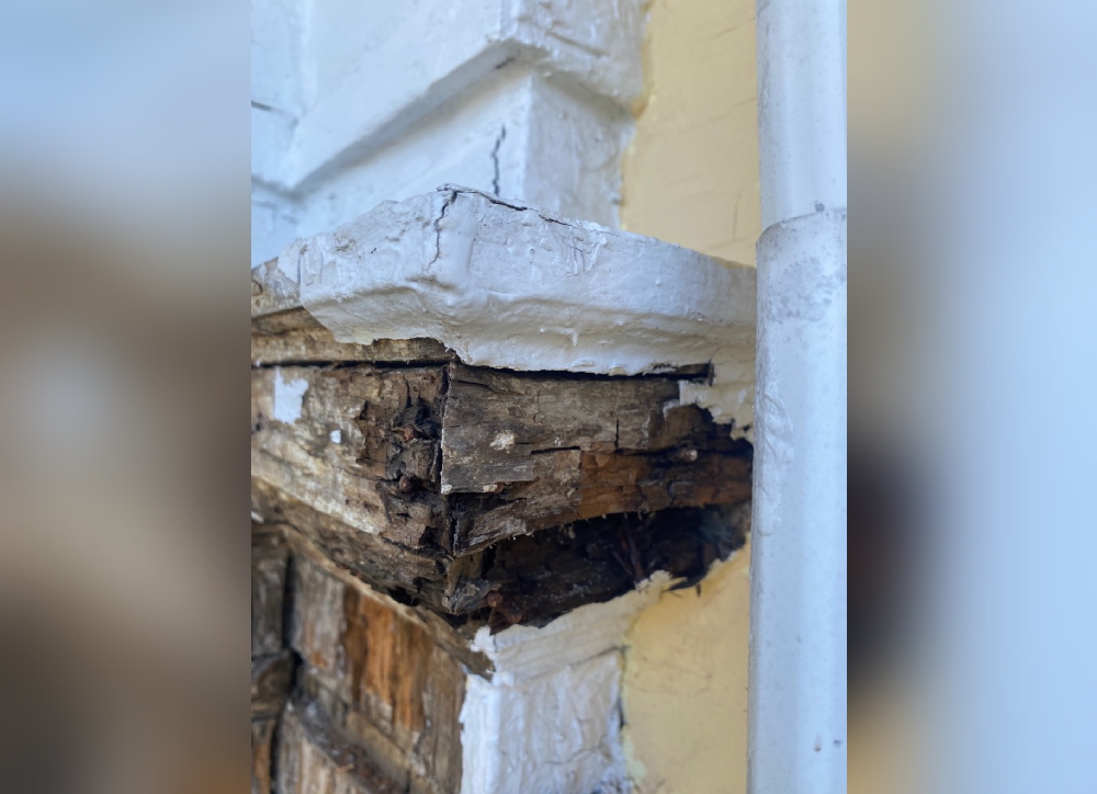Close-up of damaged wood at a column corner, highlighting rot and deterioration needing repair.