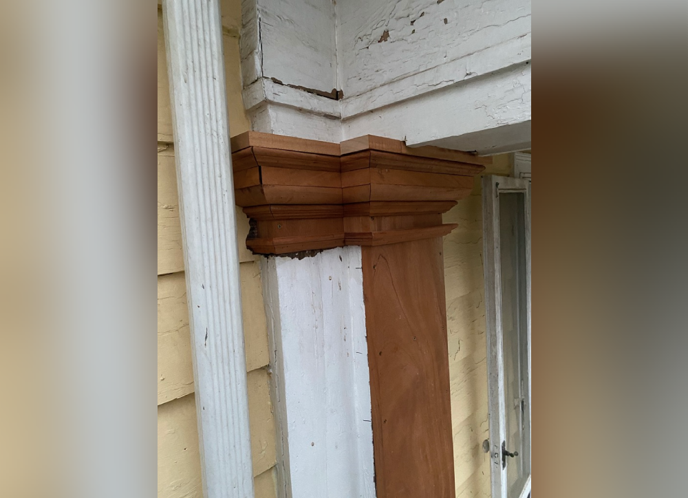 Close-up of a wooden column and porch repair detail, showcasing intricate molding and weathered paint.