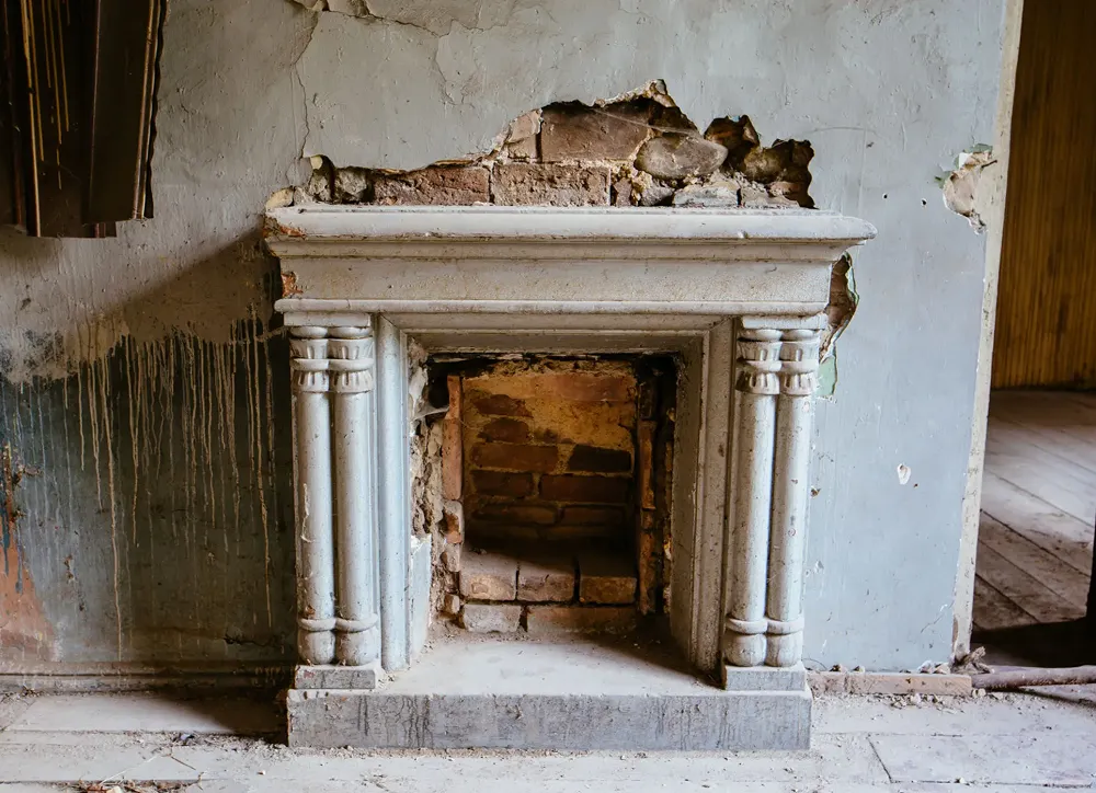 Old, damaged fireplace in a dilapidated room.
