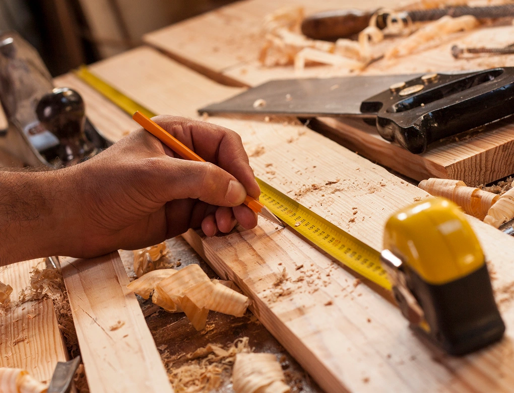 Carpenter measuring wood with yellow tape measure.
