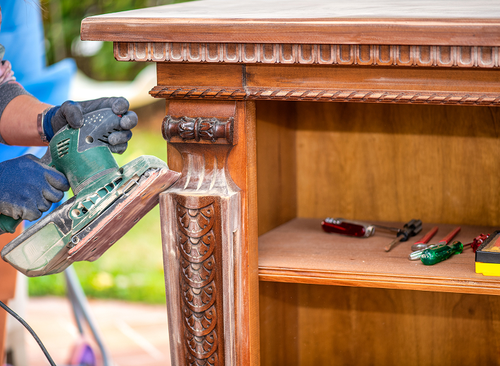 Sanding wooden furniture with electric sander.
